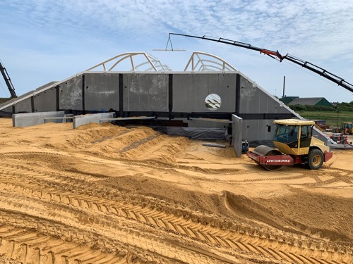 Jordopfyldningen mod bygningen, hvor geoarmeringsnet, sandfyld og en drænende komprimerbar isolering ligger lag på lag.